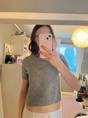 Grå stickad kortärmad tröja - Mysig grå stickad tröja med korta ärmar och ribbade kanter. Tröjan har en enkel, rak passform och är något kortare. Materialet är väldigt mjukt och bekvämt.