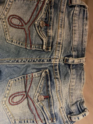 Blå slitna jeans med röd söm - Säljer ett par ljusblå jeans ifrån Gina tricot med slitningar på benen och unika bakfickor med röd broderad söm. Jeansen har klassisk femficksmodell, bälteshällor och knappgylf. Materialet är denim i bomull och passformen är rak. Jag som har xs i vanliga fall tycker dom passar (finns inspänningar/utspänningar i midjan)