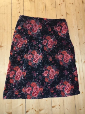 Blommig kjol med rosor romantisk - Supersnygg kjol med svart bas och stora röda och rosa rosor. Kjolen har en rak passform och är perfekt för dig som vill sticka ut lite extra. Materialet känns mjukt och följsamt, sammetkänsla.