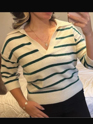 Vit stickad tröja med gröna ränder - Snygg stickad tröja i vitt med gröna horisontella ränder och krage. Tröjan har en djupare v-ringning och långa ärmar. Perfekt för en trendig och avslappnad look. Kolla min profil för fler plagg! 🥰