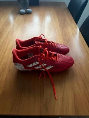 Röda Adidas fotbollsskor - Säljer ett par röda fotbollsskor från Adidas med klassiska vita ränder på sidan. Vill rensa ut lite här hemma nu så vill mest bli av med dom, dom har fungerat oerhört bra och dom har hjälpt till med många vunna skytteligor!