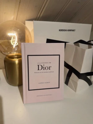 Lilla boken om Dior av Karen Homer - Säljer denna snygga Diorbok som är ljusrosa. Boken handlar om Dior och deras modehistoria. Perfekt för dig som gillar mode och vill ha en snygg bok som inredning. 