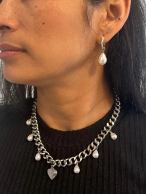 Silvrigt halsband i rostfritt stål 9 mm bredd med droppformade pärlor - Stilrent och elegant halsband i silvrig ton med vackra droppformade pärlor.  Matchande örhängen finns i en egen annons och det finns  även i guldpläterad variant.  Material: rostfritt stål och ABS (Akrylnitril Butadien Styren ) på pärlimitationen   Bredd: 9 mm Längd: Justerbar 38–43 cm Övrigt: Nickelfritt och handgjort