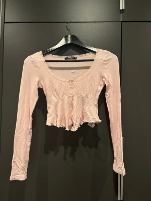 Ljusrosa topp med volang - Söt rosa topp från Gina Tricot med lång ärm och volangkant nedtill. Toppen har en liten rosettdetalj framtill och en djup rundad urringning med skuren slits vid magen. Aldrig använd men lite skrynklig pga legat länge. 
