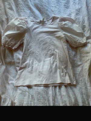 Ljusrosa topp med puffärmar från H&M - Supersöt ljusrosa topp från H&M med puffiga korta ärmar och rund halsringning. Tillverkad i mjuk bomull som känns skön mot huden. Perfekt för dig som vill ha en enkel men ändå trendig look. Knappt använd