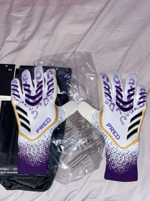Adidas Predator målvaktshandskar  - Snygga Adidas Predator målvaktshandskar i vitt, lila och guld med svarta detaljer. Storlek 8,5. Helt nya och oanvända! 
