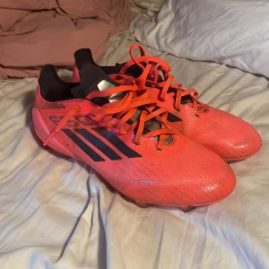 Adidas F50 fotbollsskor röd/svart - Säljer ett par Adidas F50 pro fotbollsskor i rött med svarta detaljer och klassiska tre ränder på sidan. Skorna har snörning, platt sula med dobbar och är tillverkade i syntetmaterial. Skorna har ingen som helst defekt då jag bara använt dom ett fåtal gånger pga att dom var för små. Storlek 44 men passar även 43. Kan gå ner i pris vid snabb affär. Tveka inte på att höra av dig vid någon som helst fundering.