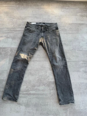 Replay Rocco grå jeans comfort fit - Säljer ett par grå jeans från Replay, modell Rocco, med comfort fit. Jeansen har klassisk femficksdesign, dragkedjegylf och snyggt tvättad look. Perfekta för dig som gillar avslappnad stil och trendiga jeans. Det ända negativa är att knappen gick sönder så fick ersätta den med en Jack and Jones knapp. Kolla gärna in mina andra replay jeans också.