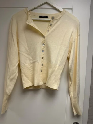 Ljusgul cardigan från Gina Tricot S  - Trendig ljusgul cardigan från Gina Tricot med långa ärmar och ribbade muddar. Koftan har en djup v-ringning och silverfärgade knappar framtill. Tillverkad i mjukt stickat material som ger en skön och avslappnad look.