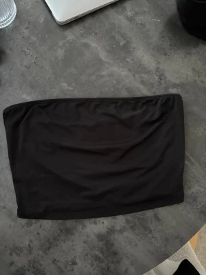 Svart bandeau tubtopp från SHEIN - En enkel och stilren svart bandeau tubtopp från SHEIN. Toppen är axelbandslös och har en tight passform som sitter snyggt på kroppen. Perfekt att matcha med höga jeans eller kjol för en clean look. Skims material 