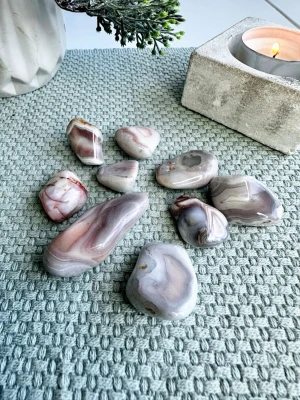 Rosa Botswana agat 9 st  - 9 st Botswana-agat med naturliga bandningar i mjuka nyanser av rosa, grått och vitt. En sten som förmedlar lugn, trygghet och emotionell balans. Botswana-agat är känd för att stötta vid stress, sorg och inre omställning – perfekt när man vill landa i hjärtat och skapa stabilitet i känslolivet.  ✨ Egenskaper (spirituellt): – Jordande men samtidigt mjuk och tröstande – Stärker självkänsla och emotionell läkning – Hjälper till att släppa oro och gamla mönster  