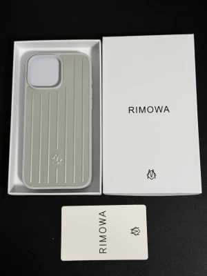 Rimowa Silver iPhone 16 Pro Max mobilskal - Stilrent mobilskal från Rimowa i silvergrå färg med ikoniska räfflade linjer och diskret logga. Skalets material känns robust och exklusivt, perfekt för dig som vill ha en snygg och skyddande look till mobilen. Passar dig som gillar minimalistisk design och premiumkänsla. För iPhone 16 Pro Max