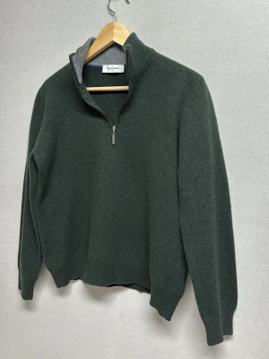 Mörkgrön halvzip från Gran Sasso - Snygg mörkgrön stickad tröja från Gran Sasso med halvzip och hög krage. Insidan av kragen är grå och mjuk, vilket ger en schysst kontrast. Perfekt till höst och vinter, tillverkad i ull för extra värme. För de som undrar består denna tröja av 80% Virgin Wool, 10% Kashmir och 10% Viscosa