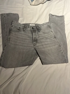 Grå raka jeans från Jack n jones  - Säljer ett par grå jeans från Jack n jones med rak passform och klassisk femficksdesign. Jeansen har hög midja och är tillverkade i ett mjukt denimtyg. Perfekta för en avslappnad och trendig look. Bara höra av dig vid frågor.