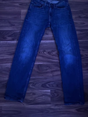 Mörkblå jeans från Dressmann - Snygga mörkblå jeans från Dressmann med klassisk femficksdesign och raka ben. Jeansen är tillverkade i bomull med en bekväm passform. Perfekta för en stilren och avslappnad look.