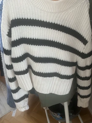 Randig stickad tröja från Gina Tricot - Säljer en vit stickad tröja från Gina Tricot med svarta horisontella ränder. Tröjan har rund halsringning, långa ärmar och ribbade muddar. Perfekt för dig som gillar en klassisk och avslappnad stil.