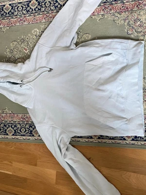 Ljusgrå hoodie med magficka - Säljer en enkel och clean ljusgrå hoodie med stor magficka och justerbar huva med snören. Hoodien har långa ärmar och är tillverkad i mjukt bomullstyg, perfekt för en avslappnad och chill stil.