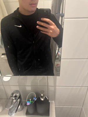 Nike Zip - Snygg svart träningsjacka från Nike med dragkedja framtill och vit logga på bröstet. Jackan har hög krage och är tillverkad i ett lätt och stretchigt material som passar perfekt till träning eller uppvärmning. Använt 2 gånger, som ny! Nypris: 600