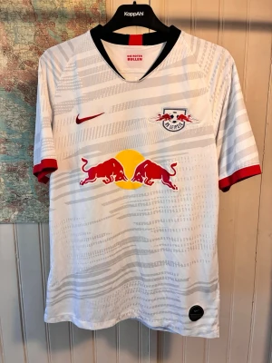RB Leipzig Nike 2016/17 kit, size M - Good condition.  #nike #rbleipzig #bundesliga #germany #keita #werner #forsberg #sabitzer #poulsen  Vit RB Leipzig fotbollströja med klubbmärket och Nike-loggan på bröstet. Tröjan har ett mönster i grått och rött på ärmarna.