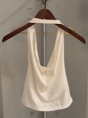 Zara topp  - Säljer en stilren vit halterneck linnetopp med draperad framsida. Toppen är ärmlös och har en öppen rygg, perfekt för varma dagar. Enkel att matcha med både jeans och kjol.