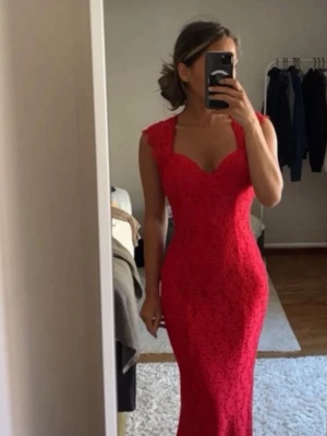Röd lång spetsklänning med öppen rygg - Snygg röd långklänning i spets med figurnära passform och öppen rygg. Klänningen har breda axelband och en djup urringning framtill. Perfekt för bal eller student. Materialet är spets med fina detaljer.