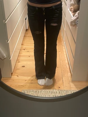 Svarta bootcut jeans weekday med slitningar - Säljer ett par svarta bootcut jeans med egengjorda slitningar. Jeansen har låg midja och utsvängda ben.