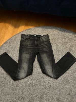 Svarta skinny  jeans från Jack & Jones - Säljer ett par svarta skinny jeans från Jack & Jones med snyggt slitna detaljer och klassisk femficksmodell. Jeansen har en tvättad look med grå toner och raka ben. Perfekta för en avslappnad och trendig stil.