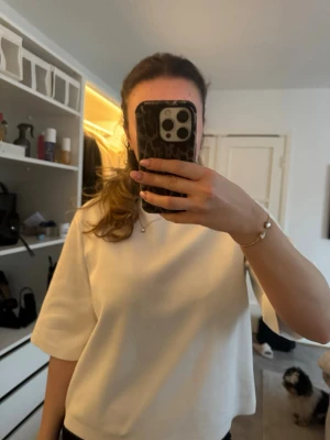 Vit croppad topp med halvlånga ärmar - Säljer en stilren vit topp med croppad passform och halvlånga ärmar. Toppen har en enkel och clean design, perfekt att matcha med både jeans och kjol. Materialet är lite tjockare.