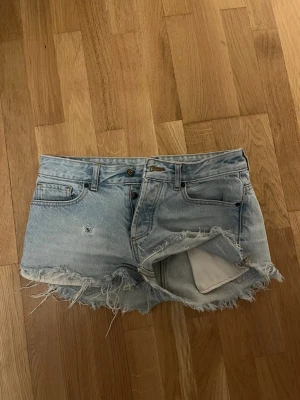 Ljusblå lågmidjade jeansshorts från Topman - Säljer ett par ljusblå skinny jeansshorts från Topman med fransiga kanter och slitna detaljer. Klassisk femficksmodell med knappgylf. Perfekta och supersnygga till sommaren.