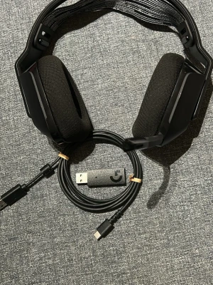 Svarta gaminghörlurar Logitech G - Säljer ett par svarta trådlösa gaminghörlurar från Logitech G-serien. Hörlurarna har stora, mjuka öronkuddar i tyg och justerbart huvudband i plast och metall. Inkluderar USB-dongel och laddkabel med USB-C. Perfekta för gaming och streaming.