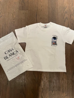 Vit t-shirt från Casablanca med tryck - Vit t-shirt från Casablanca med färgglatt tryck av palmer och stadsmotiv både fram och bak. Klassisk passform och rund hals. Perfekt för dig som gillar stilrena plagg med unika detaljer.