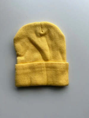 Gul ribbstickad mössa - En enkel och stilren gul mössa i ribbstickad klassisk modell med uppvikt kant som ger en avslappnad look. Perfekt för att addera färg till din outfit.