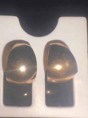 Chunky guldfärgade örhängen från UR&penn - Säljer ett par chunky örhängen i guldfärgad metall. De har en rundad, halvbågig form och en blank, polerad yta som ger en cool och modern look. Perfekta för dig som gillar statement-smycken och vill addera lite extra bling till din stil.