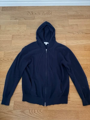 Mörkblå kashmir-mix ziphoodie - Mörkblå kashmir-mix zip-hoodie från Barlucio med hel dragkedja framtill, huva med dragsko och två fickor. Tillverkad i ett mjukt stickad kashmir-mix som ger en avslappnad och stilren look. Perfekt för lager-på-lager och enkel att matcha med jeans. Lite nopprig därav det låga priset annars i fint skick.Tveka inte på att höra av dig vid frågor kring passform eller fler bilder på plagget! Storlek S.