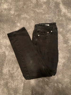 Svarta Jeans Jack and Jones | W29 - Snygga svarta jeans från Jack and Jones  i Loose fit-modell. Klassisk femficksdesign med knappgylf och silverfärgade nitar. Jeansen är tillverkade i stretchigt denimtyg som ger en bekväm passform och en modern look.