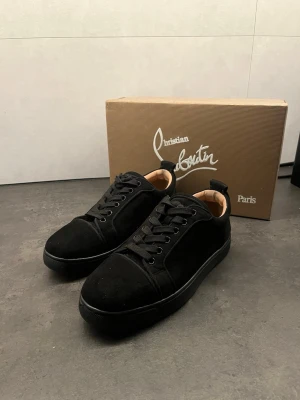 Svarta sneakers från Christian Louboutin - Stilrena svarta sneakers från Christian Louboutin med klassisk röd sula. Skorna har ovandel i mocka och läderdetaljer, svarta skosnören och låg profil. Perfekta för dig som vill ha en clean och exklusiv look. Priset kan diskuteras! Skorna är 39 men sitter som 41