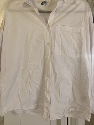 Vit klassisk skjorta från HM - Klassisk vit skjorta från HM med lång ärm, bröstficka och knappar framtill. Skjortan har en avslappnad passform och är tillverkad i bomull, perfekt för en clean och enkel stil.