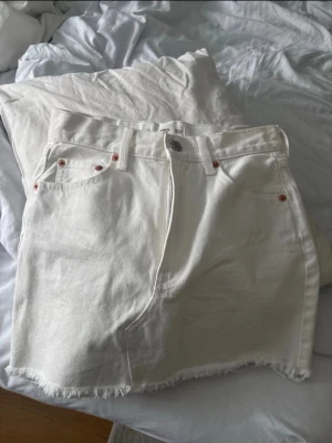 Vit jeanskjol  - Säljer en vit jeanskjol från Monki med rå, fransig nederkant och klassiska femficksdetaljer. Kjolen har knapp och dragkedja framtill samt bakfickor. Perfekt för dig som gillar en enkel och clean look.