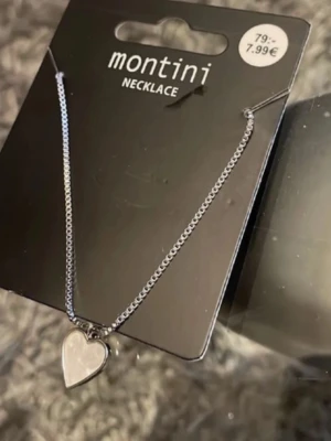 Silverfärgat halsband med hjärthänge - Snyggt halsband från Montini i silverfärg med ett stilrent hjärthänge. Kedjan är tunn och elegant, perfekt för att ge en söt touch till din outfit. Passar dig som gillar minimalistiska smycken och hjärtformade detaljer.