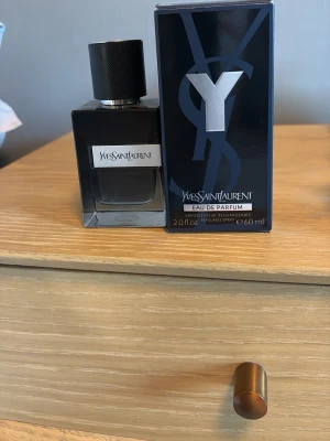 Yves Saint Laurent Y Eau de Parfum - Y Eau de Parfum från Yves Saint Laurent i en elegant, mörkblå glasflaska med svart lock. Flaskan har en stilren, fyrkantig form och en metallisk etikett med loggan. Förpackningen är också mörkblå med en stor silverfärgad Y-detalj. Volymen är 60 ml. Ungefär 40 kvar av 60ML