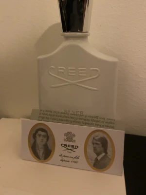 Creed Silver Mountain Water parfym - Exklusiv parfym från Creed i modellen Silver Mountain Water. Flaskan är vit med silverfärgad kork och har en elegant, stilren design med Creed-loggan i relief. Perfekt för dig som gillar lyxiga och fräscha dofter.