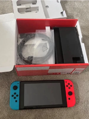 Nintendo Switch med neonröda och blå Joy-Con - Ingår några spel!!‼️‼️Nintendo Switch spelkonsol med neonröda och blå Joy-Con-kontroller. Konsolen har en rektangulär form med svart kropp och färgglada handkontroller. Medföljer gör dockningsstation, HDMI-kabel och originalkartong. Perfekt för gaming både hemma och på språng.