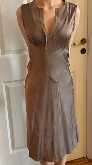 Klänning från Filippa K - Elegant klänning i siden med djup v-ringning och ärmlös design. Klänningen har en mjuk glans och följsam passform som ger en lyxig känsla. Perfekt för dig som gillar minimalistisk och stilren look.