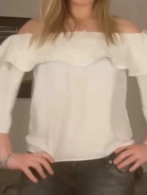 Vit offshoulder topp med volang - Säljer en stilren vit offshoulder topp med bred volang runt axlarna. Toppen har trekvartsärm och en rak passform som ger en fräsch och trendig look. Perfekt att matcha med jeans eller kjol för en snygg outfit.