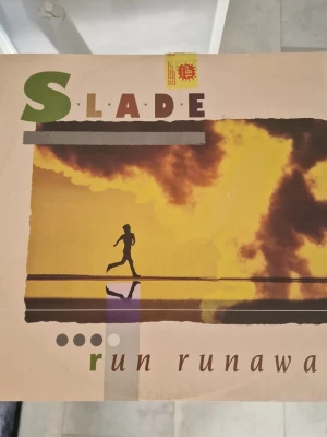 Slade - Run Runaway vinylsingel - Vinylsingel med omslag från bandet Slade, låten 'Run Runaway'. Omslaget har en siluett av en springande person mot en gul och brun bakgrund med moln. Text och grafiska detaljer i grönt, brunt och lila. Perfekt för samlare av klassisk rock. Inga repor.