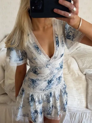 GUESS blommig kortklänning med spetsdetaljer - Säljer denna söta GUESS kortklänning med blått blommönster. Klänningen är v-ringningad med spetsdetaljer längs kanterna och har korta ärmar. Skriv vid frågor!💕pris går att diskutera vid snabb affär 🫶