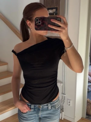 Svart off shoulder body - Trendig svart offshoulder body med tight passform och kort ärm. Snygg asymmetrisk skärning över axlarna. 