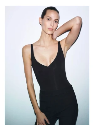 Zara Svart body med djup urringning - Snygg svart body med djup v-ringning och smala axelband. Tight passform som framhäver siluetten. Perfekt att styla med jeans eller kjol för en trendig look.