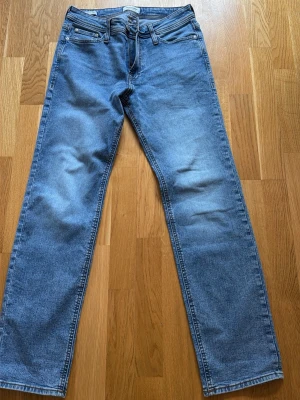 Blå raka jeans från Jack & Jones - Snygga blå jeans från Jack & Jones i modellen Regular/Clark. Jeansen har raka ben, klassisk femficksdesign och ljus tvätt med subtila slitningar. Perfekta för en avslappnad och trendig look. Materialet är mjukt denim som sitter skönt hela dagen.