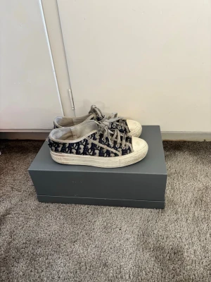 Dior Walk'n'Dior Sneakers  - Säljer mina klassiska Walk'n'Dior sneakers i det ikoniska blå Dior Oblique broderade canvas-mönstret. En tidlös lyxsneaker som passar till allt! Detaljer: • Märke: Christian Dior • Modell: Walk'n'Dior • Mönster: Oblique Embroidery • Detaljer: Signaturer på skosnören, tungan och sulan ("Christian Dior J'Adior").  